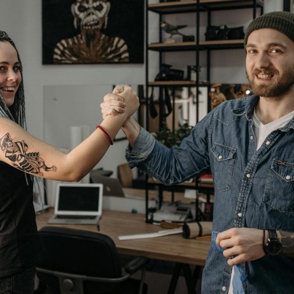 A cheerful moment between a man and woman with tattoos indoors, shaking hands and smiling.